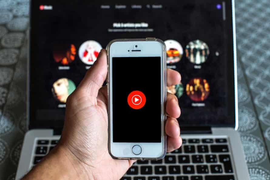 تلفن را با دست در مقابل لپ‌تاپ نگه می‌دارید که هر دو برنامه موسیقی YouTube را نمایش می‌دهند