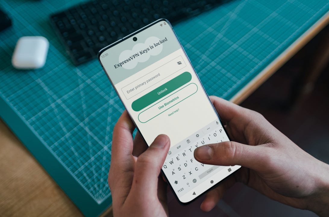 A pair of hands hold a mobile device displaying the two-button login screen for ExpressVPN's password manager, Keys.