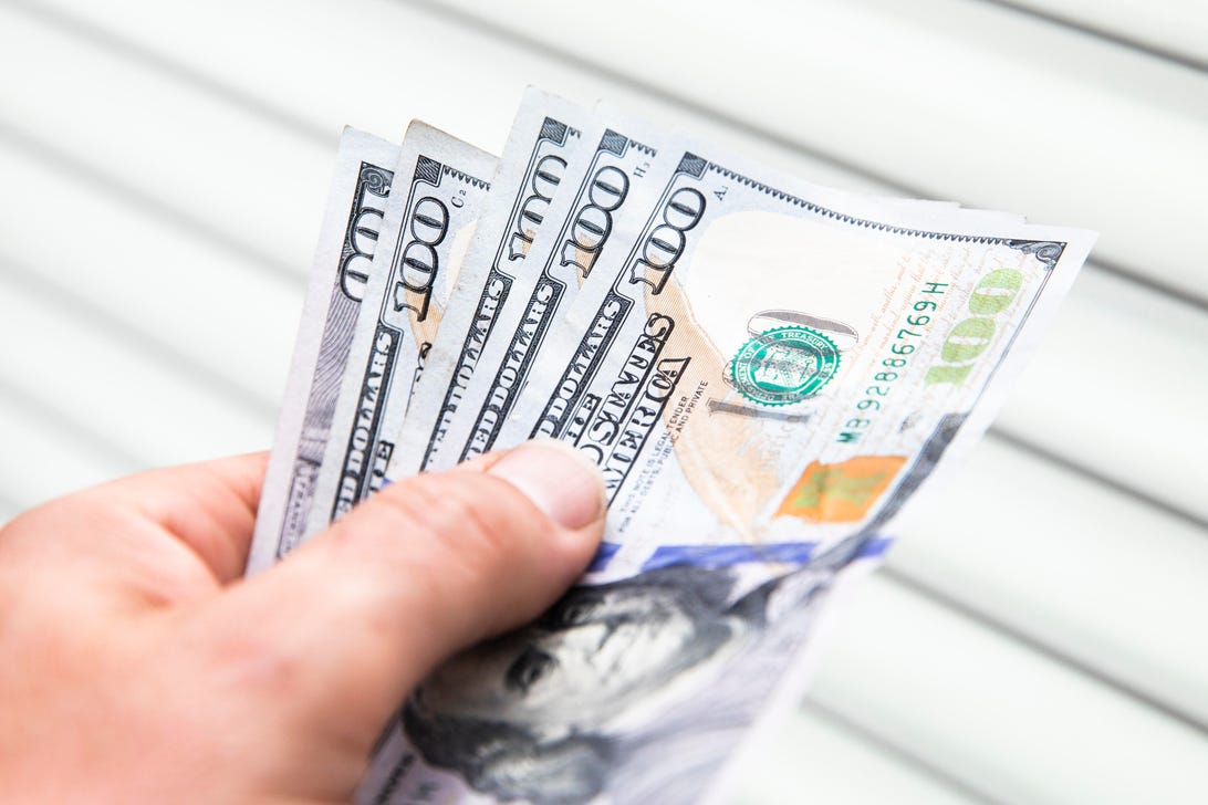A hand holding five $100 bills