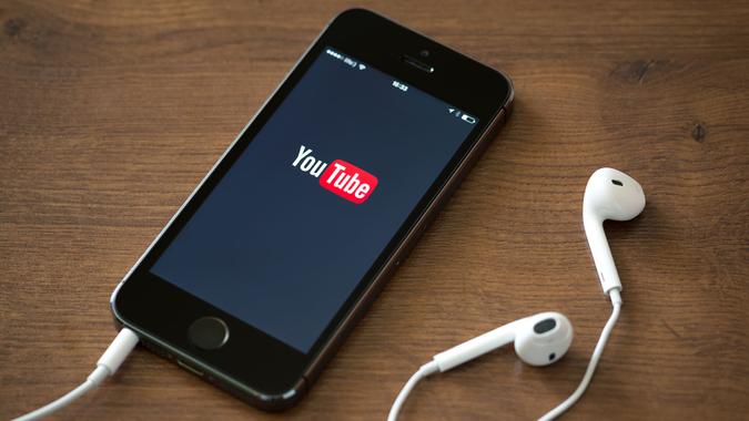 Kiev, Ukraine - June 5, 2014: Brand new Apple iPhone 5S with YouTube application service on the screen lying on a desk with headphones.