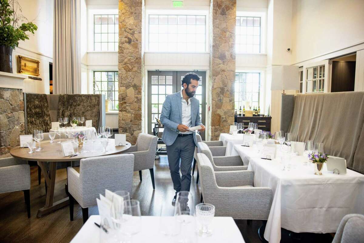 Top photo: Founded in 1972, Clos du Val Winery unveiled a new luxurious, glass-walled hospitality center in 2018, adjacent to the original winery and tasting room (pictured). Ruben Moreno, above, prepares the tasting room at Heitz Cellar in St. Helena, which reopened following an extensive remodel this year.